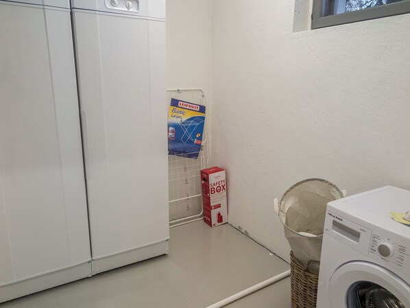 A laundry room with a washing machine, a safety box, and a Leifheit product on the wall.