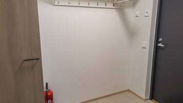 A room with a white wall, a door, a fire extinguisher, and a coat rack.