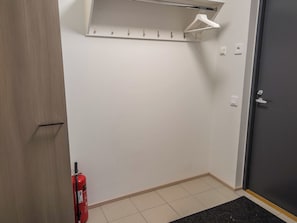 Een kamer met een witte muur, een deur, een brandblusser en een kapstok.