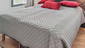 Una cama bien hecha con una colcha gris acolchada y tres almohadas rojas.
