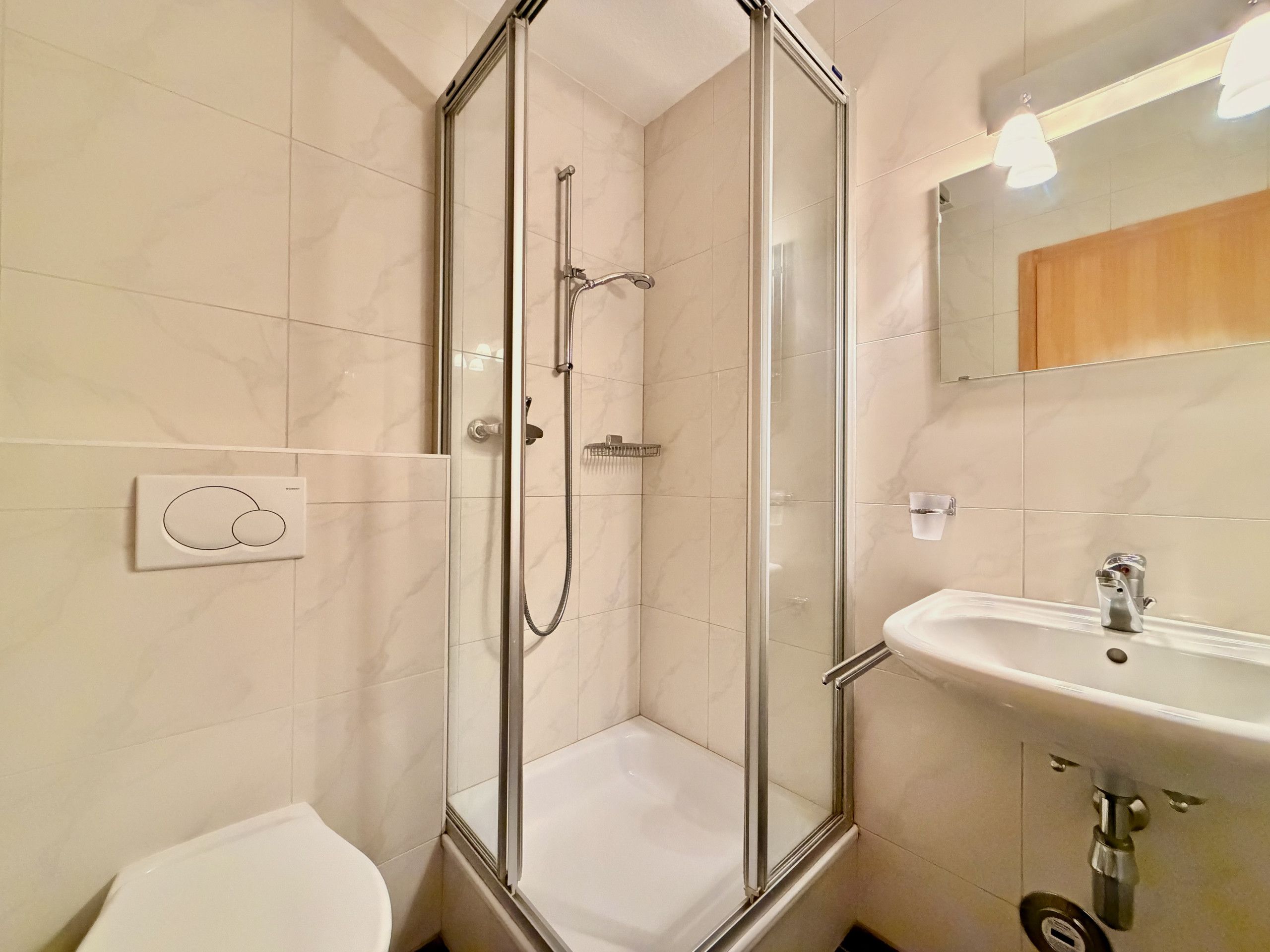 Een moderne badkamer met een douchecabine van glas, een witte wastafel en een toilet.