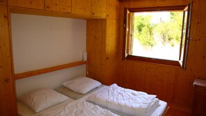 Una habitación con dos camas individuales, paredes de madera, una ventana con vistas a follaje y un armario pequeño.