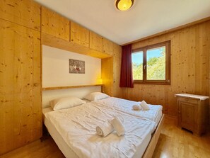 Una habitación con paneles de madera, una cama, una mesita de noche y un ventanal con cortinas.