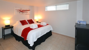 A neatly made bed with red pillows, two bedside lamps, and a window with blinds.