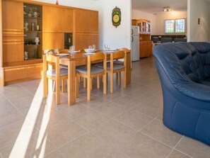 Un comedor con sillas de madera y una mesa dispuesta para cuatro, un sofá azul y una cocina al fondo.