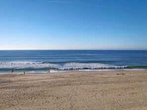 Ein weiter Sandstrand mit sanften Wellen und blauem Himmel.