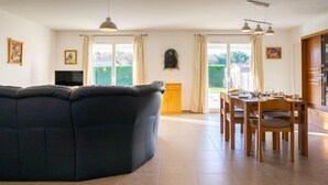 En rummelig opholdsstue med en mørk sofa, et spisebord med stole og et køkkenområde.