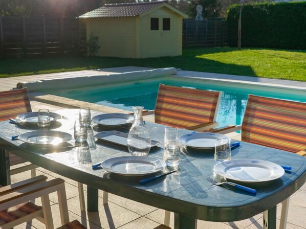 Mesa de comedor al aire libre con piscina de fondo.