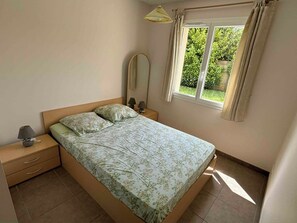 Un dormitorio con cama, mesitas de noche, una ventana con cortinas y vistas a zonas verdes.