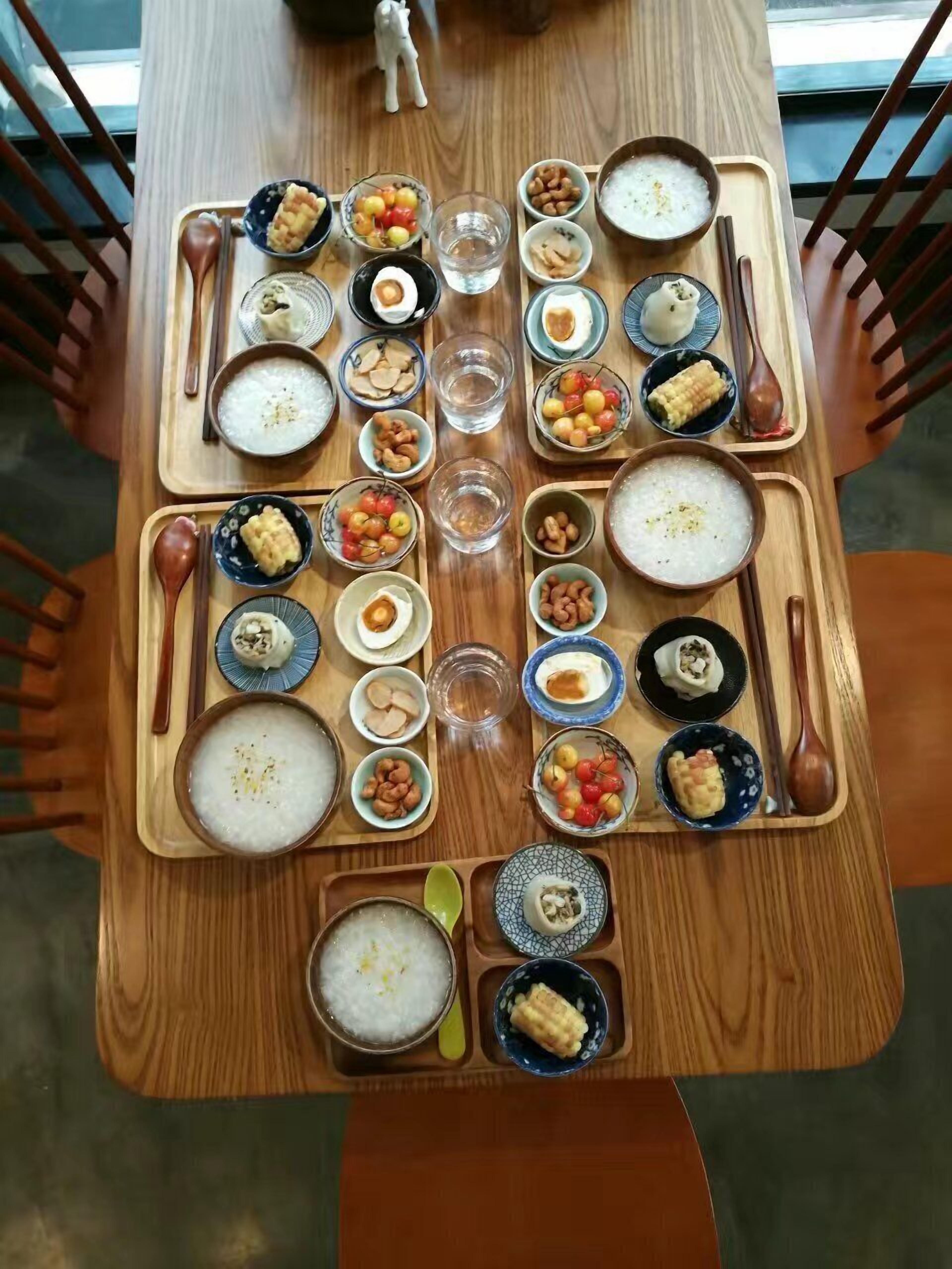 A wooden dining table with various dishes and utensils, including bowls of rice, vegetables, and meat, arranged for a meal.