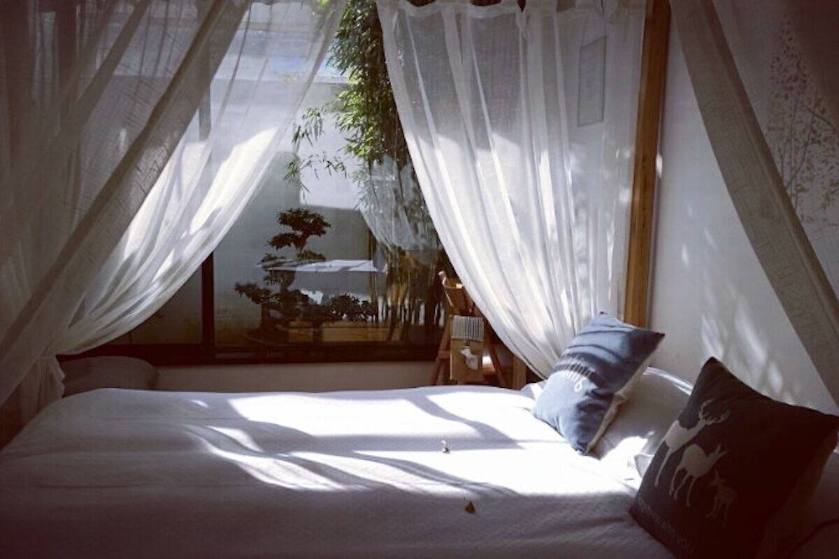Una cama con ropa blanca, un almohadón azul y un dosel con cortinas traslúcidas.