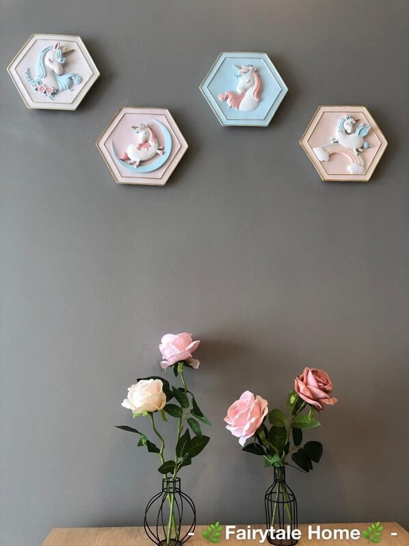 Una pared decorada con arte mural hexagonal que muestra unicornios y un jarrón con rosas rosadas.