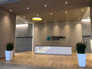 Un área de recepción con diseño moderno, que presenta un techo de madera, un gran letrero con el nombre "WINDMILL" y dos plantas en macetas.