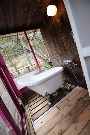 Une salle de bain en bois avec une baignoire sur pieds, une douche et une fenêtre donnant sur un jardin.