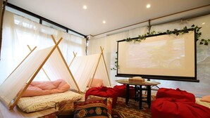 A cozy room with a projector screen, a small table, and comfortable seating including a red bean bag and patterned cushions. - WOOD DESIGN PARK - Campground (Okazaki)