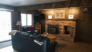 A living room with a fireplace, a sofa, a television, and a window. - Ausable River  Cottage (Frederic)