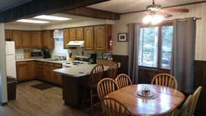 A kitchen with wooden cabinets, a stove, a microwave, and a dining area with a table and chairs. - Ausable River  Cottage (Frederic)