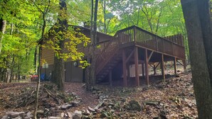 Eine Holzhütte mit einer Holzdiele und Treppe, umgeben von Bäumen und Felsen.