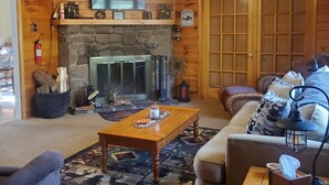 Ein gemütliches Wohnzimmer mit Kamin aus Stein, Deckenventilator und Wandfernseher.
