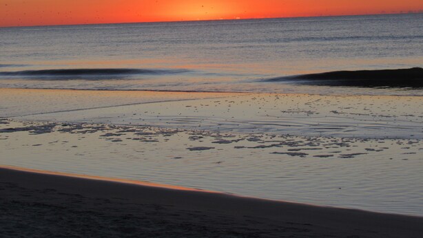 Una playa con un atardecer sobre el océano.