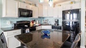 A modern kitchen with white cabinets, a black refrigerator, stainless steel appliances, and a granite countertop. - RENOVATED BEACHSIDE Condo-Elevator-Heated Pool-in unit Washer/Dryer  (Galveston)