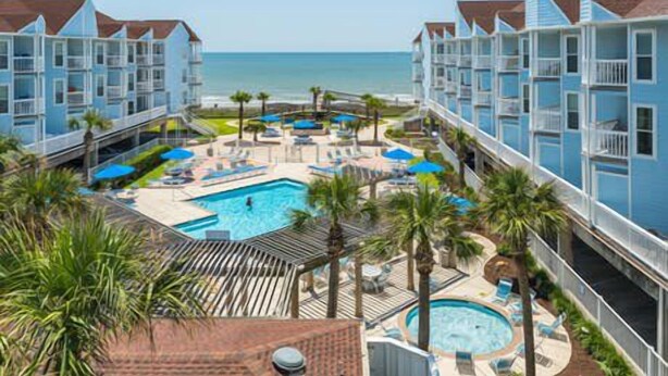 A hotel with a pool area, including a hot tub, lounge chairs, and umbrellas. - RENOVATED BEACHSIDE Condo-Elevator-Heated Pool-in unit Washer/Dryer  (Galveston)