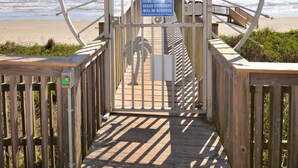 A wooden boardwalk leading to a beach with a sign warning about items left behind overnight. - RENOVATED BEACHSIDE Condo-Elevator-Heated Pool-in unit Washer/Dryer  (Galveston)