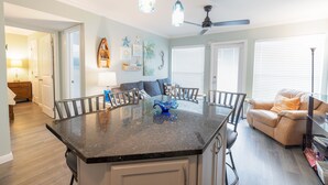 A kitchen with a central island, dining chairs, a ceiling fan, and a living area with a sofa and blinds. - RENOVATED BEACHSIDE Condo-Elevator-Heated Pool-in unit Washer/Dryer  (Galveston)