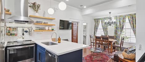 Una cocina moderna con electrodomésticos de acero inoxidable, una isla central y un comedor con candelabro y cortinas estampadas.