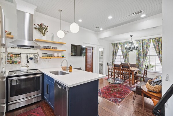 A modern kitchen with stainless steel appliances, a central island, and a dining area with a chandelier and patterned curtains. - View of St Charles Avenue from the balcony! (New Orleans)