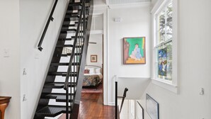 Un escalier menant à une chambre à coucher où se trouvent un lit et un tableau coloré accroché au mur.