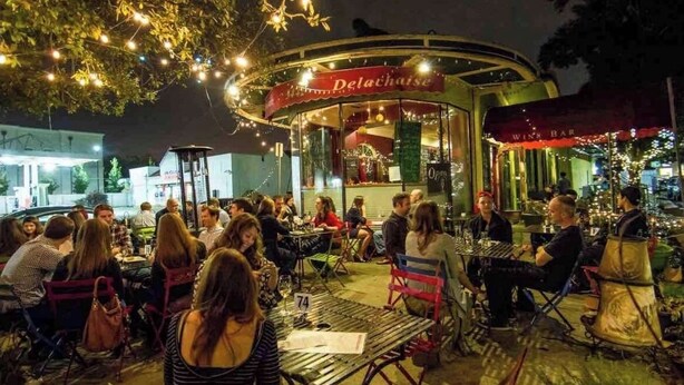 Un espace extérieur aménagé avec des tables et des chaises, une enseigne indiquant « Delaoise », et un bar à vin en arrière-plan.
