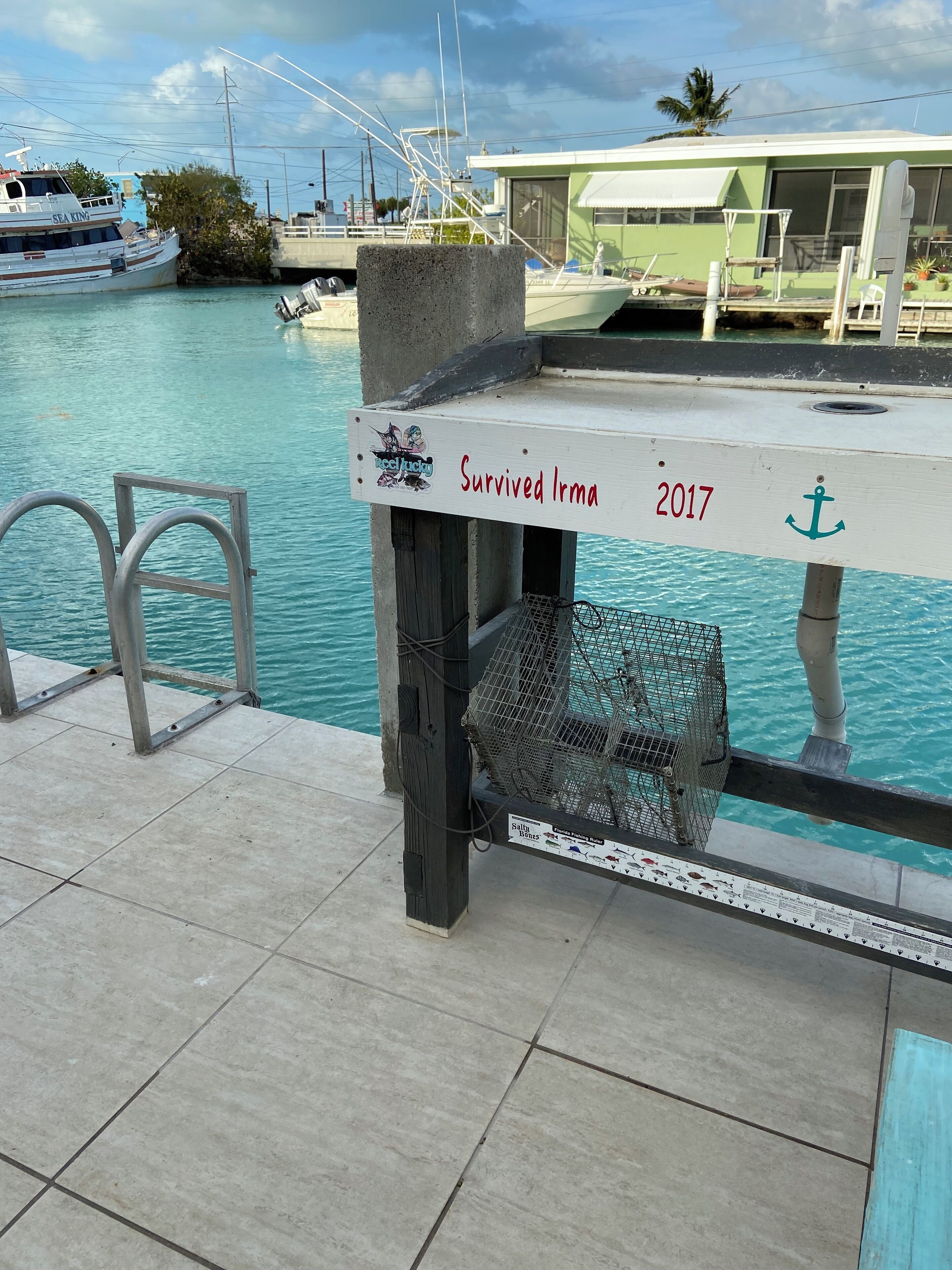 Um cais com uma placa que diz "Sobreviveu a Irma 2017" e um barco de pesca ao fundo.