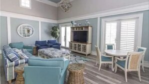 A living room with a sectional sofa, a TV cabinet, and a dining area with chairs and a table. - CB334 Romantic & Family Ocean & Golf Views - & bring your pet too! (Palm Coast)