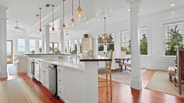 A spacious kitchen with white cabinetry, a large island, pendant lighting, and a view of the outdoors. - Beach Lawn Cottage: Premier Oceanfront Escape | Amazing Views | Steps to Beach | Beachfront Pools (Saint Simons Island)