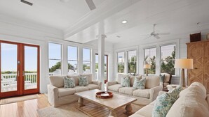 A spacious living room with a large wooden coffee table, two beige sofas with patterned cushions, and a wooden cabinet. - Beach Lawn Cottage: Premier Oceanfront Escape | Amazing Views | Steps to Beach | Beachfront Pools (Saint Simons Island)