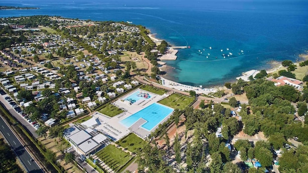 Vue aérienne d’une station balnéaire dotée d’une grande piscine, d’une plage et de nombreux petits chalets situés en bord de mer.