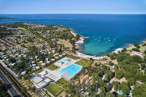 An aerial view of a coastal resort with multiple bungalow-style accommodations, a central swimming pool, and a beach area. - Mobilehome with terrace by the pool (Umag)