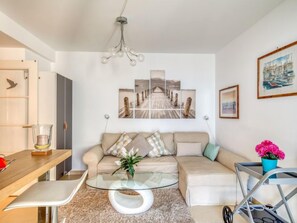 A modern living room with a glass coffee table, beige sofa, and a wooden dining table.