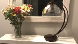 Una consola blanca con un jarrón de flores, una lámpara y cestas de mimbre.