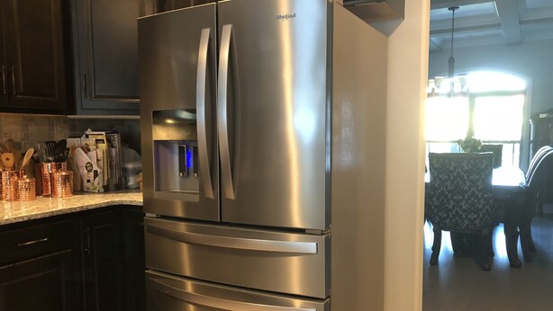 Un refrigerador de acero inoxidable en una cocina con armarios oscuros y una encimera.