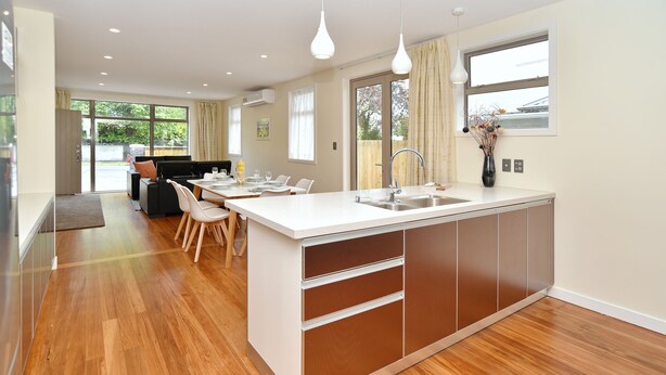 A modern kitchen with a central island, stainless steel appliances, and a dining area with chairs and a table. - Clyde 106 (Christchurch)