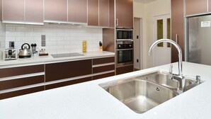 A modern kitchen with stainless steel appliances, a double sink, and brown cabinetry. - Clyde 106 (Christchurch)