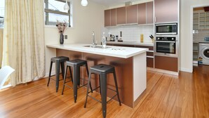 A modern kitchen with a central island, bar stools, a sink, and built-in appliances. - Clyde 106 (Christchurch)