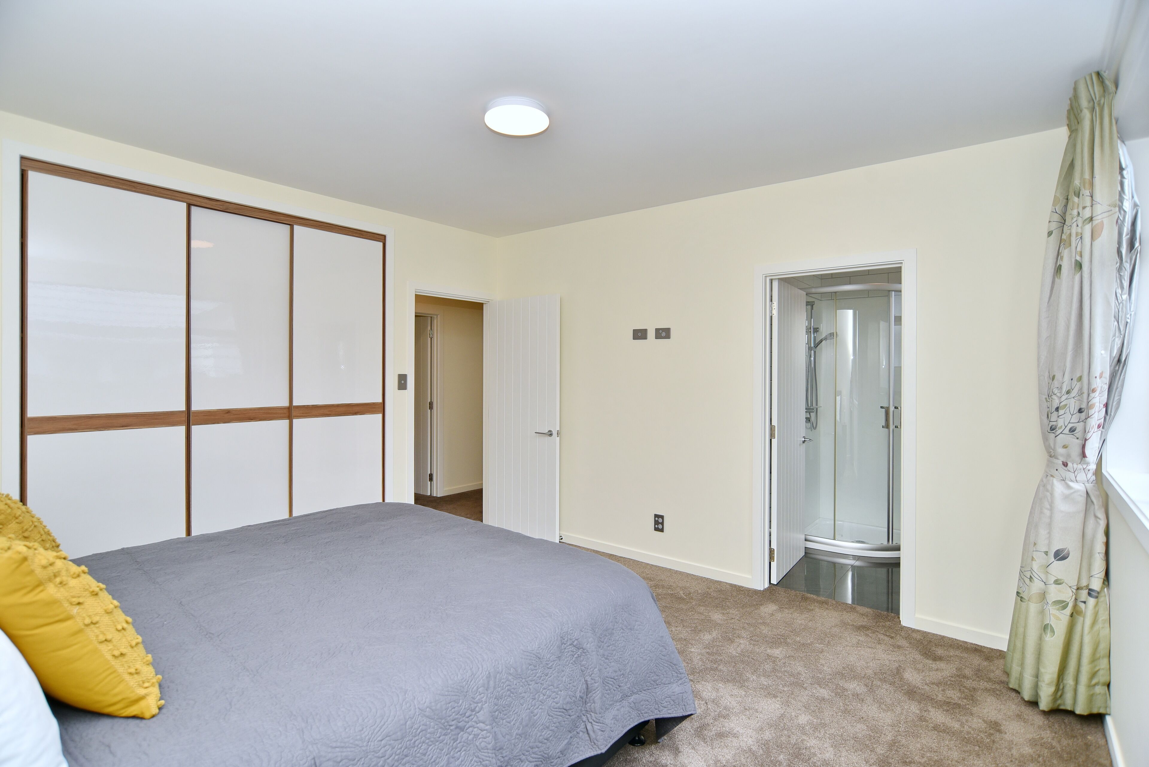 Ein Schlafzimmer mit Bett, begehbarem Kleiderschrank, Dusche und einem Fenster mit Vorhängen.