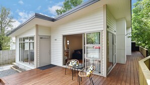 A modern house with a deck, a sliding glass door, and a small patio area with two chairs and a table. - Clyde 106 (Christchurch)