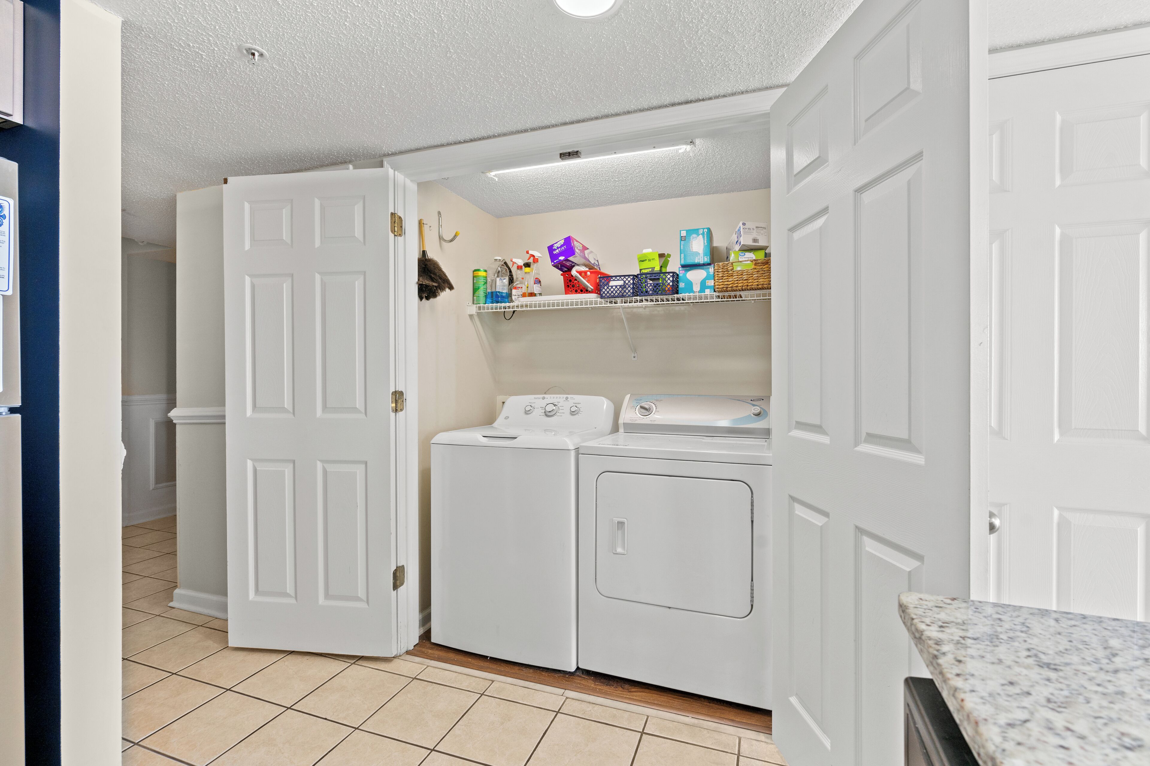 A laundry room with a washing machine, dryer, and shelves with cleaning supplies.