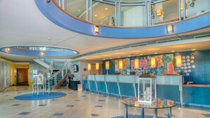 A modern hotel lobby with a curved staircase, a reception desk, and a glass table. - Avista Resort 720 - 3 Bedroom Oceanfront Condo with Lots of Amenities! (NORTH MYRTLE BEACH)