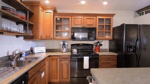 A kitchen with wooden cabinets, a stainless steel sink, a black stove, a microwave, and a refrigerator. - Snowcrest, Hot tub!  Walk to lifts! (Mt. Crested Butte)