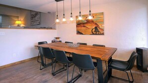 A dining area with a wooden table, black chairs, pendant lights, a painting, and a speaker. - Snowcrest, Hot tub!  Walk to lifts! (Mt. Crested Butte)